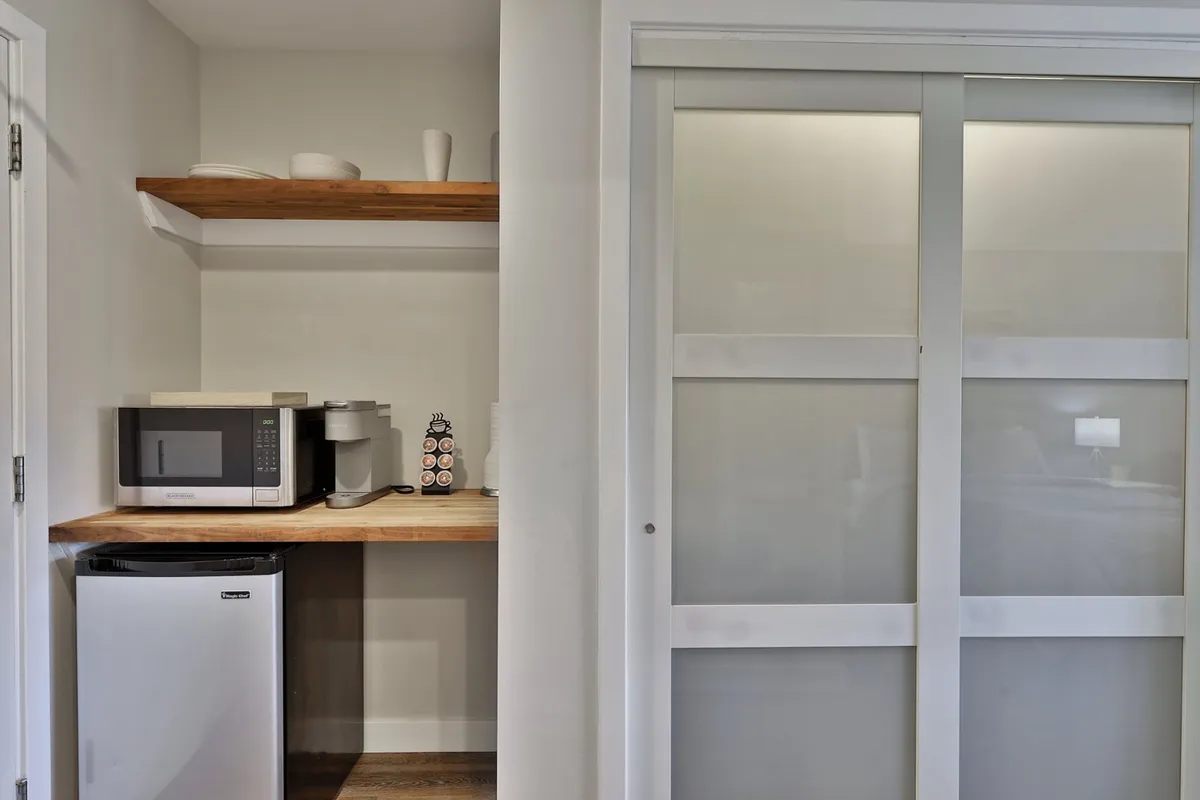 A cozy nook showcasing the kitchenette with a microwave, coffee maker, and shelves. The scene emphasizes convenience, with easy access to appliances and a comfortable atmosphere for a quick snack or coffee break.