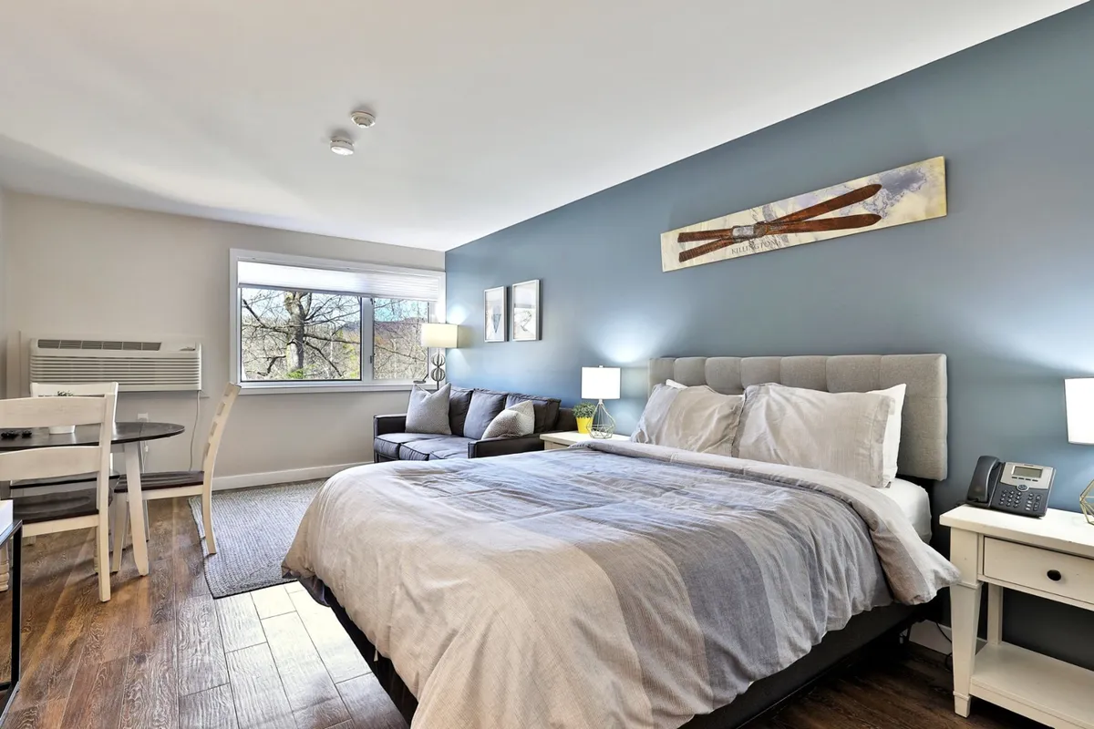 This image captures the main studio area, showcasing a plush queen bed and a comfortable sleeper sofa set against tasteful artwork and a small table. The scene exudes a sense of relaxation, with soft lighting and a serene ambiance perfect for unwinding after a day outdoors.