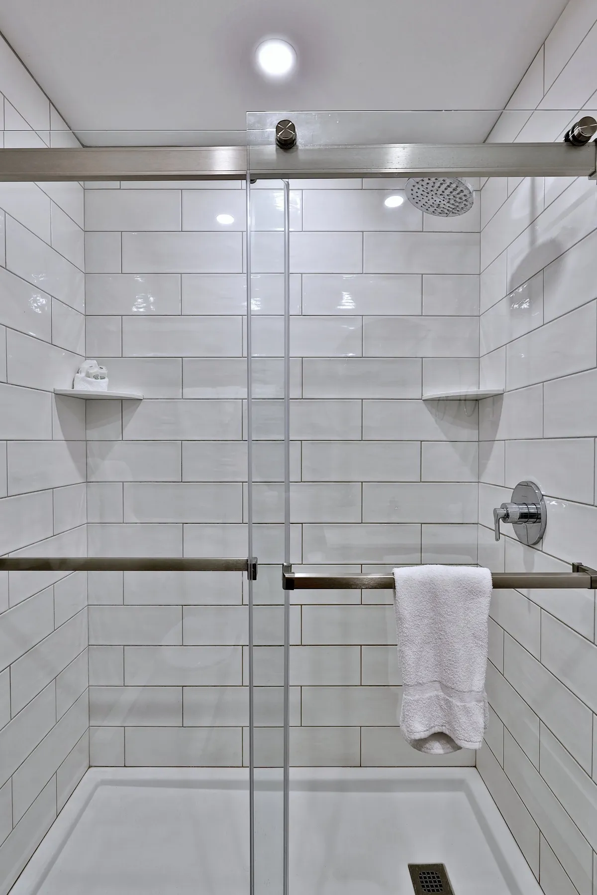 This photo features a modern glass shower enclosure with a sleek showerhead and crisp white towels. The clean lines and bright, refreshing atmosphere highlight the ensuite bathroom's contemporary design and its focus on comfort and rejuvenation.