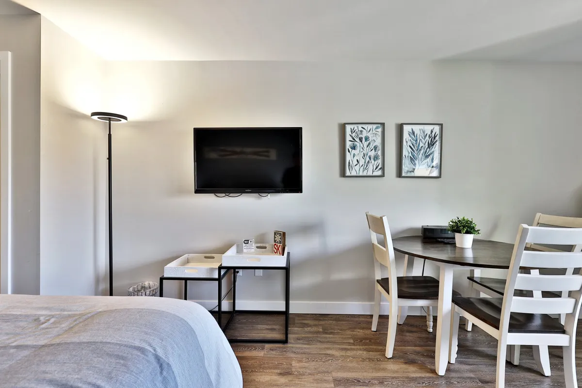 A dining/work table positioned near a wall-mounted TV, illuminated by natural light with warm, cozy decor. The setup makes it easy to imagine dining, working remotely, or enjoying leisure time in comfort.