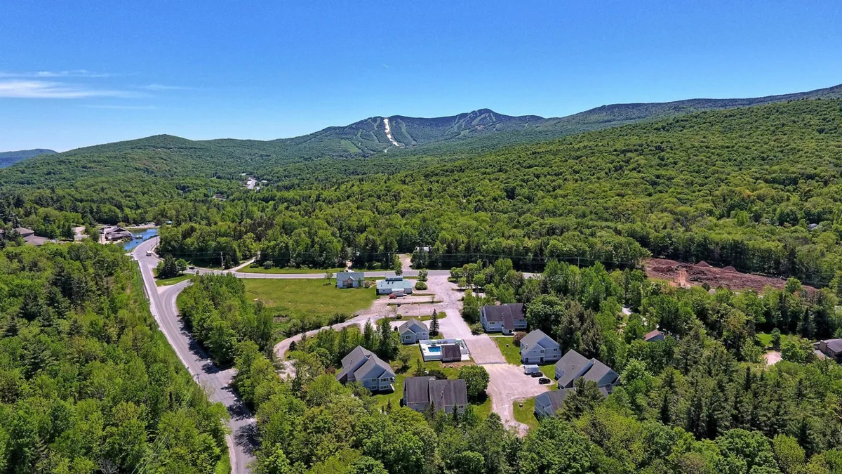 This exterior image shows a scenic mountain backdrop behind a cluster of houses, with a road leading into the community. The scene is peaceful and inviting, capturing the essence of a mountain getaway and hinting at the proximity to outdoor activities like skiing and hiking.