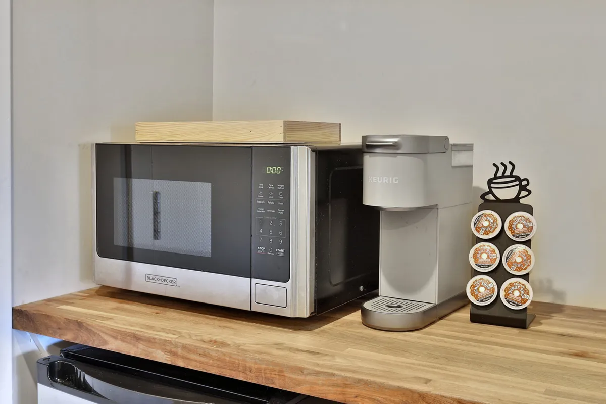 A close-up view of the kitchenette area featuring a microwave and a Keurig coffee maker on a wooden countertop. The scene is well-lit and inviting, emphasizing the convenience of meal prep and the ability to enjoy fresh coffee at any time.