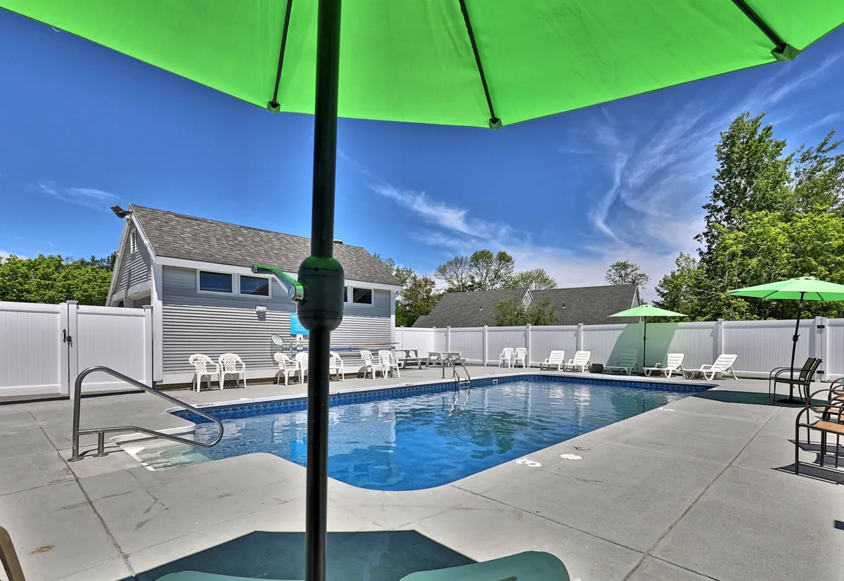 This exterior image captures a vibrant swimming pool area complete with green umbrellas and lounge chairs, set against a backdrop of greenery. The scene is lively yet inviting, suggesting a space where guests can relax, socialize, or unwind between events and local activities.